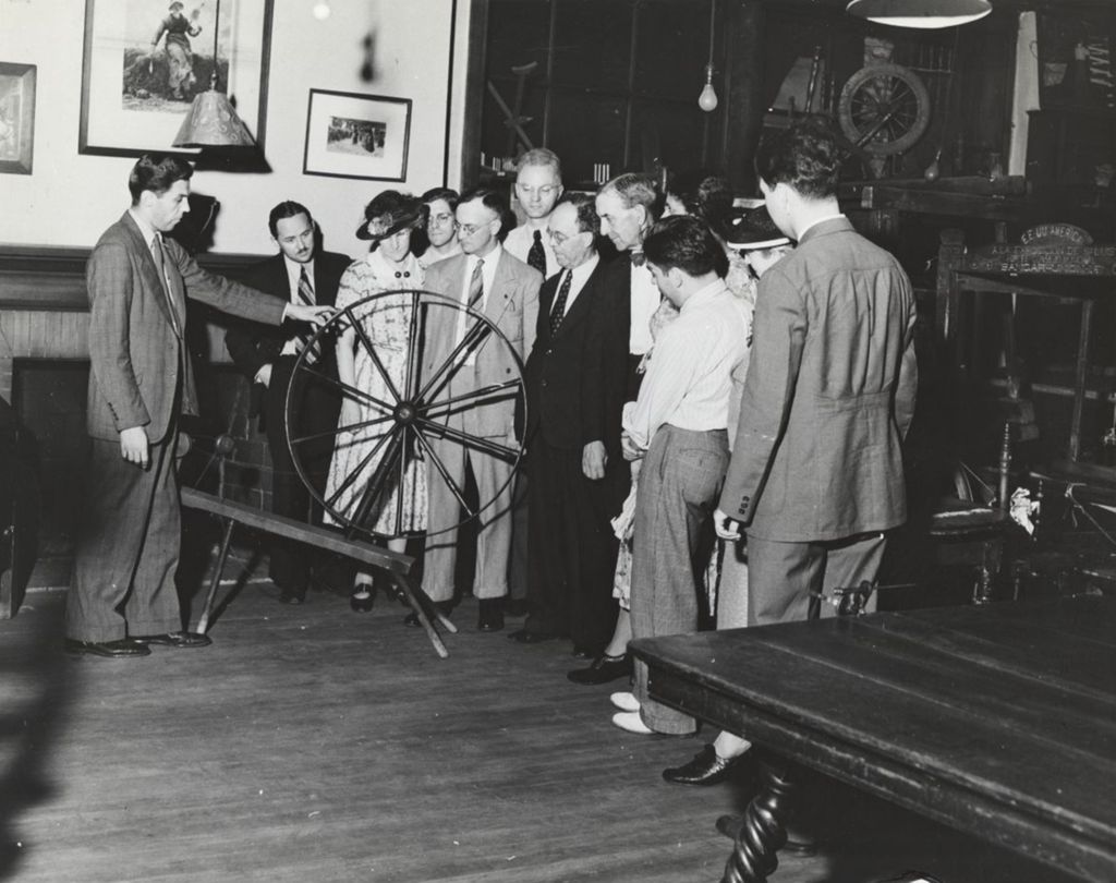 A group of visitors inspecting a large spinning wheel in the Hull-House Labor Museum