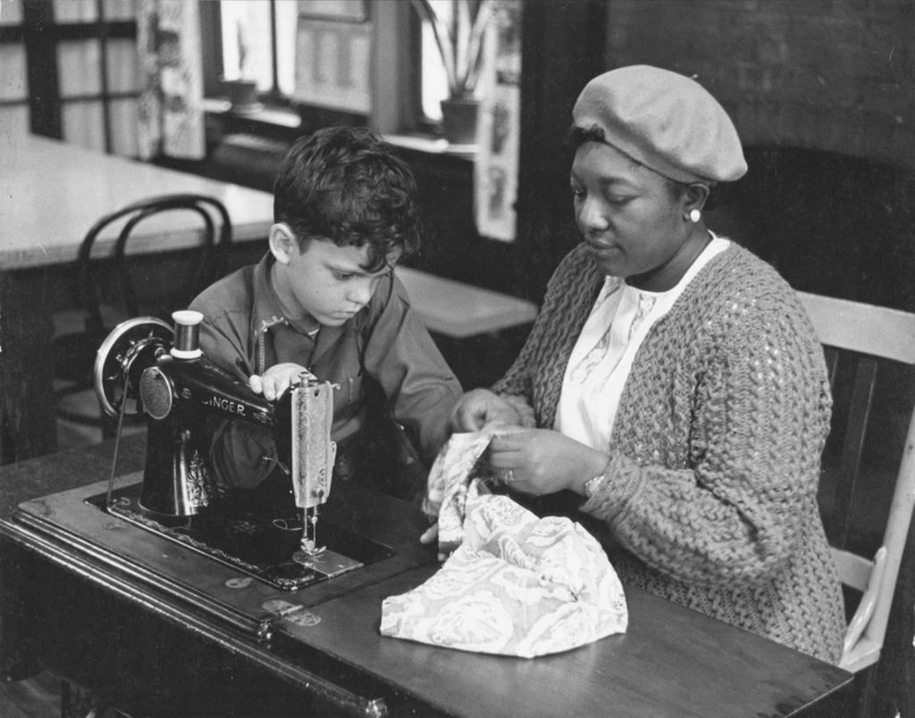 Hull-House instructor Georgia Gardner helps a boy at a sewing table