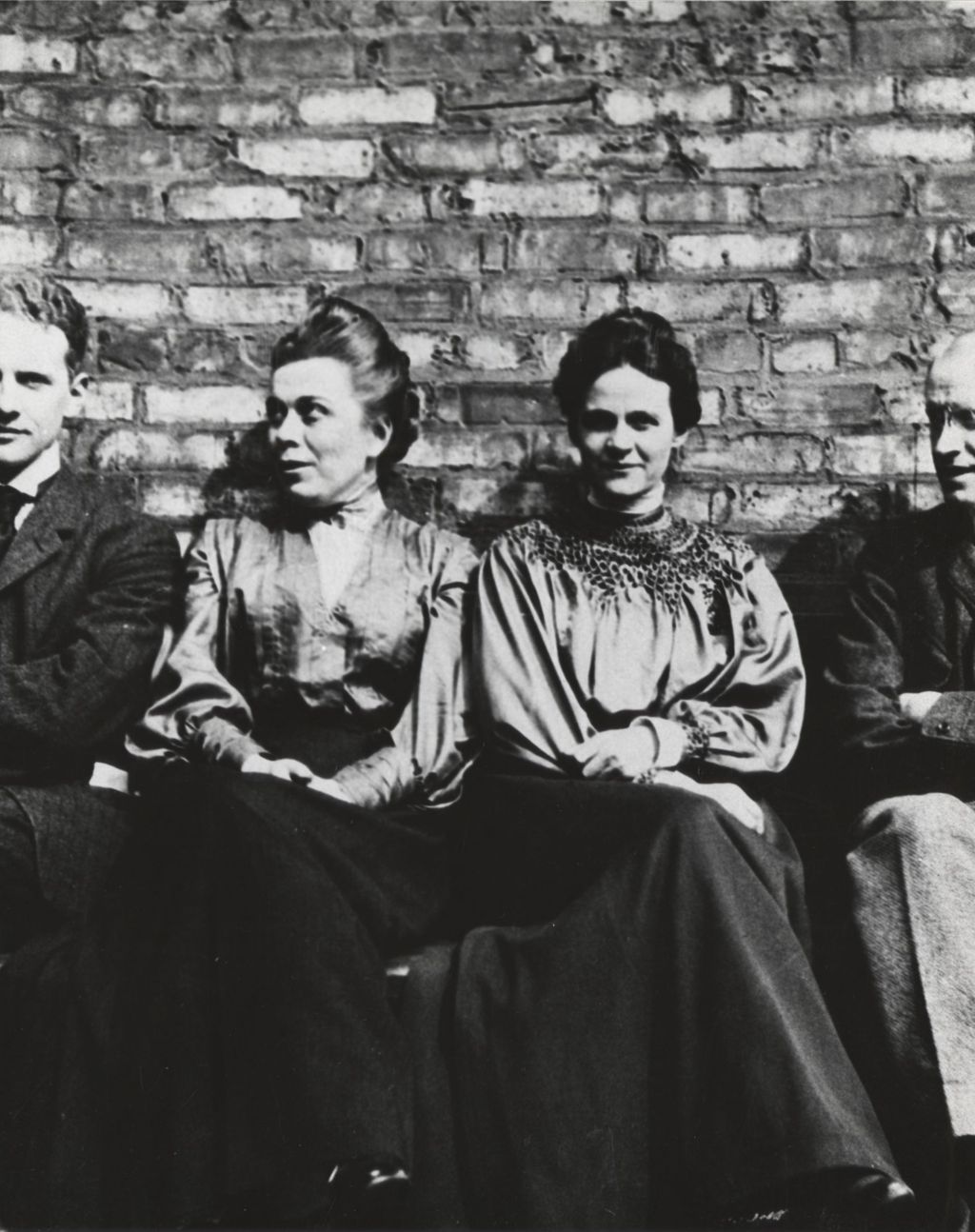 Miniature of Four people sitting on a bench against a brick wall
