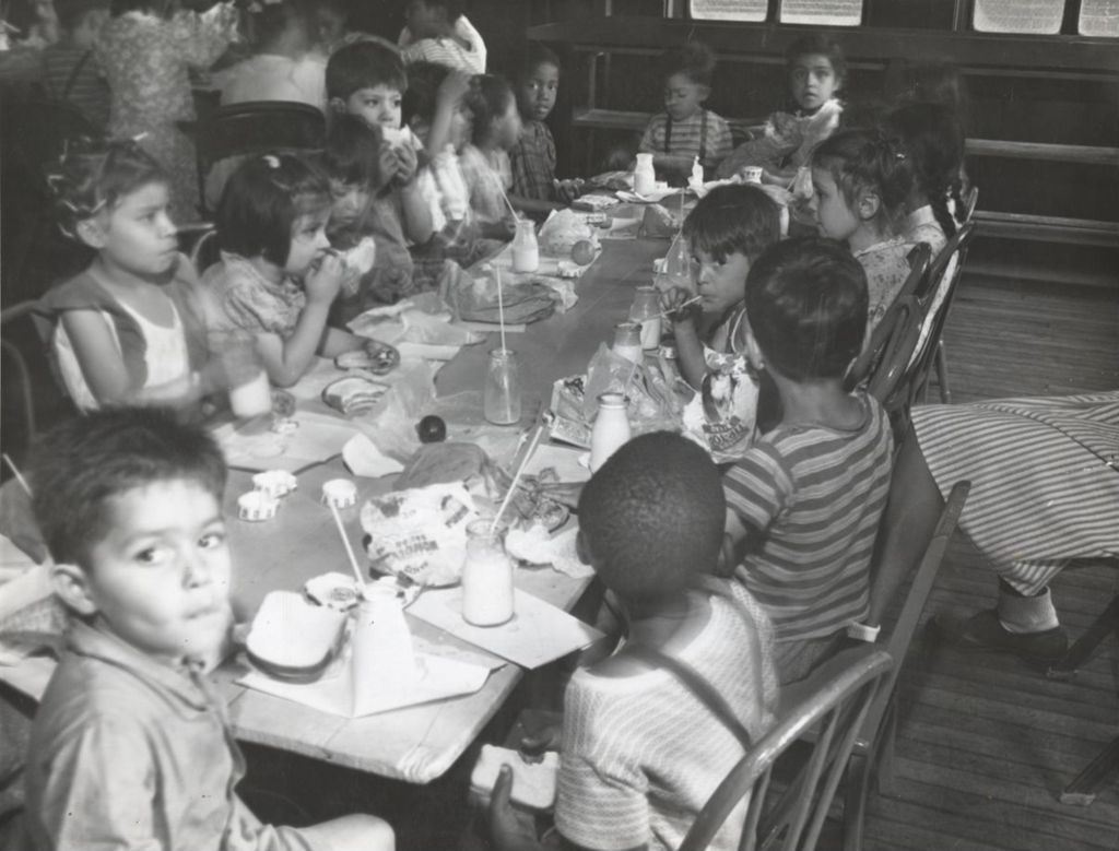 Summer play group participants sitting around a table eating lunch at Hull-House