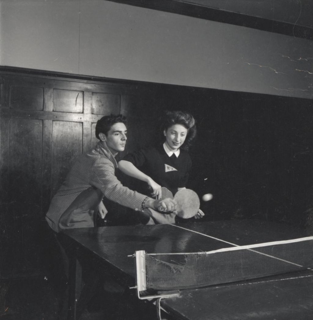 Young man and young woman playing doubles table tennis in Hull-House game room
