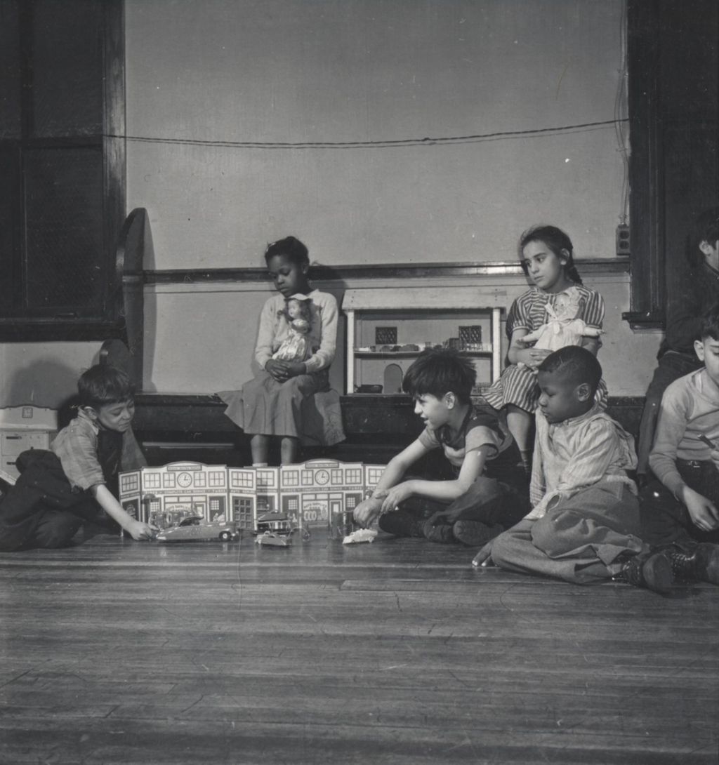 Children in a Hull-House play group with toy cars, a street scape, and dolls