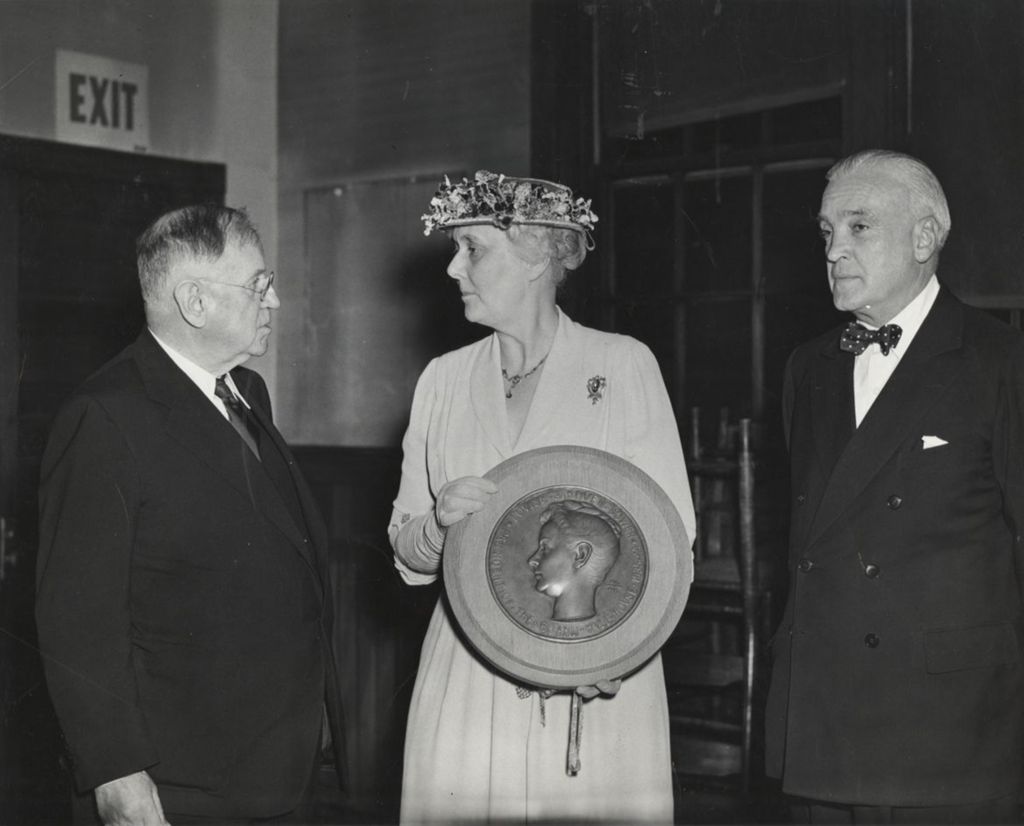 Miniature of Hull-House board president Alma Petersen stands between Harold Ickes and Marshall Field III holding a plaque honoring Louise de Koven Bowen at the 1949 Associates Dinner