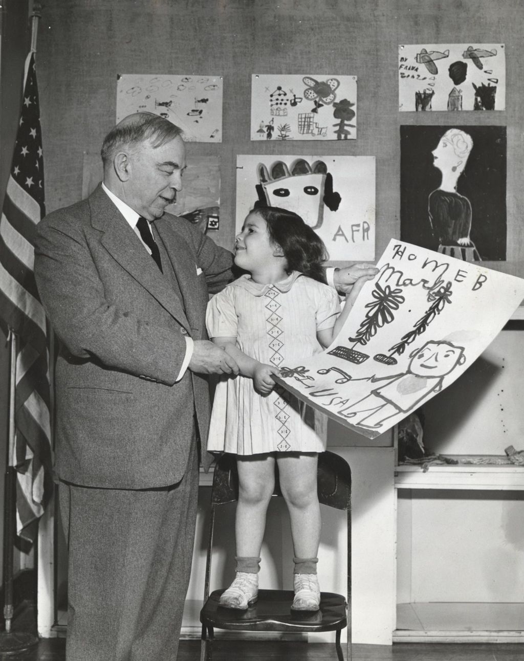 Canadian Prime Minister and former Hull-House resident W. L. Mackenzie King poses with a girl standing on a chair holding up her artwork