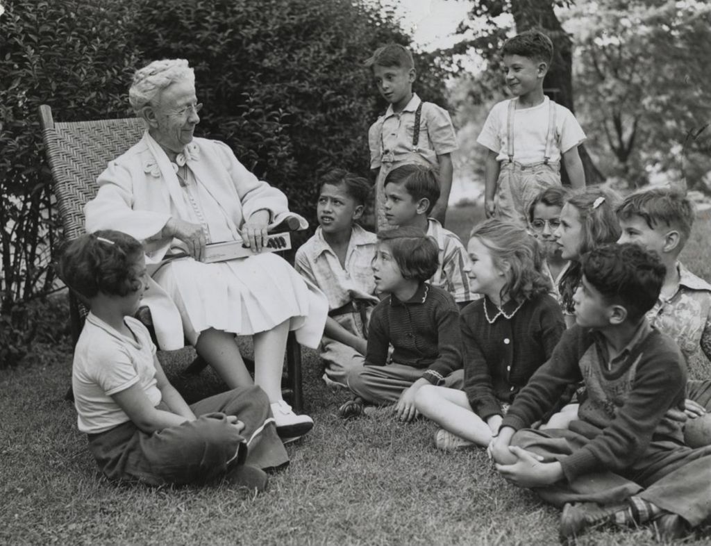 Louise de Koven Bowen sitting in a chair on the lawn of Bowen Country Club surrounded by children
