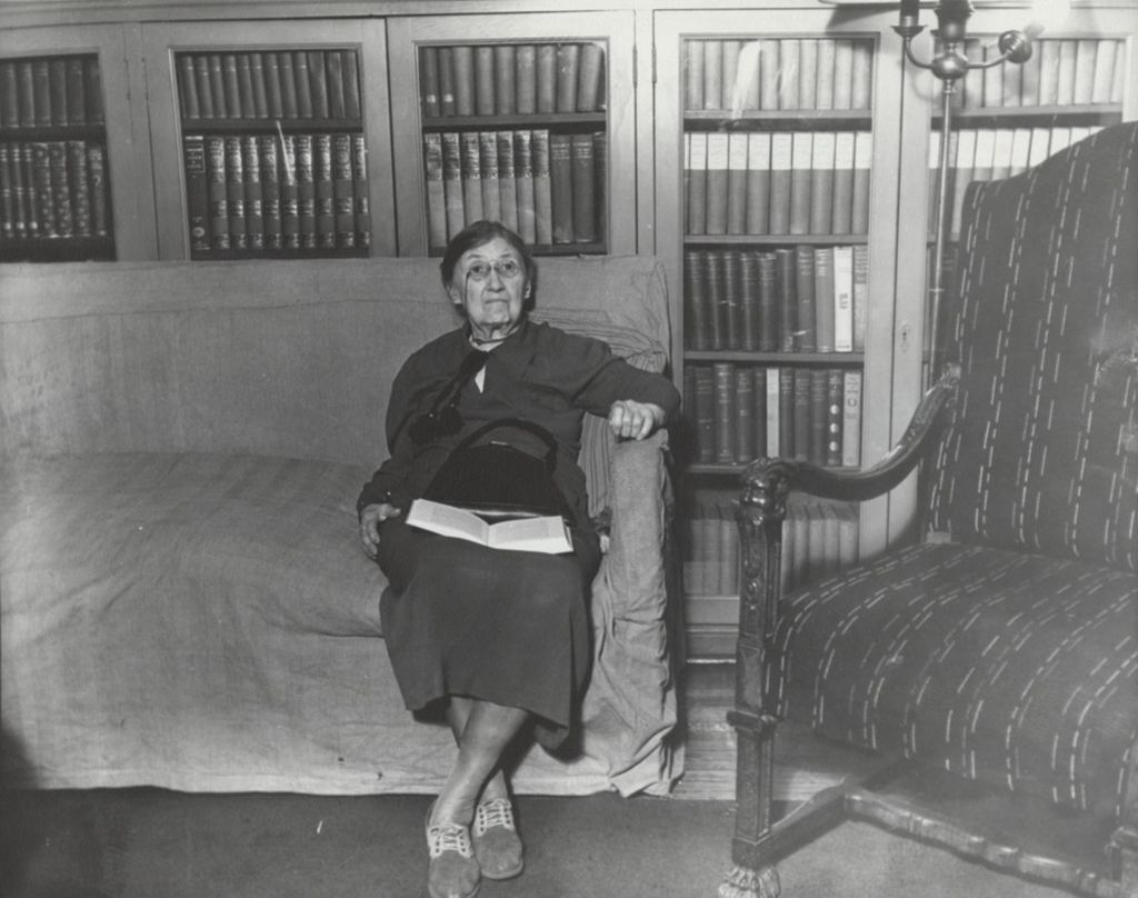 Miniature of Hull-House Art School founder and director Enella Benedict sitting on couch in a library at Hull-House