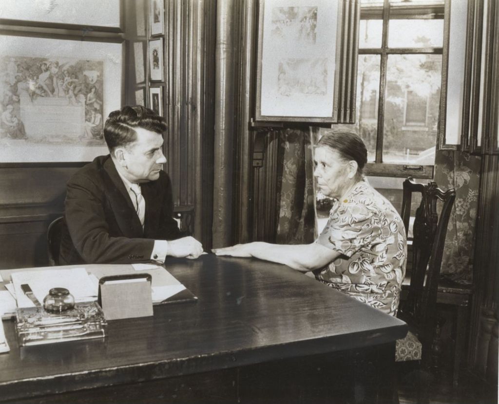 Hull-House Head Resident Russell W. Ballard at his desk with woman from neighborhood