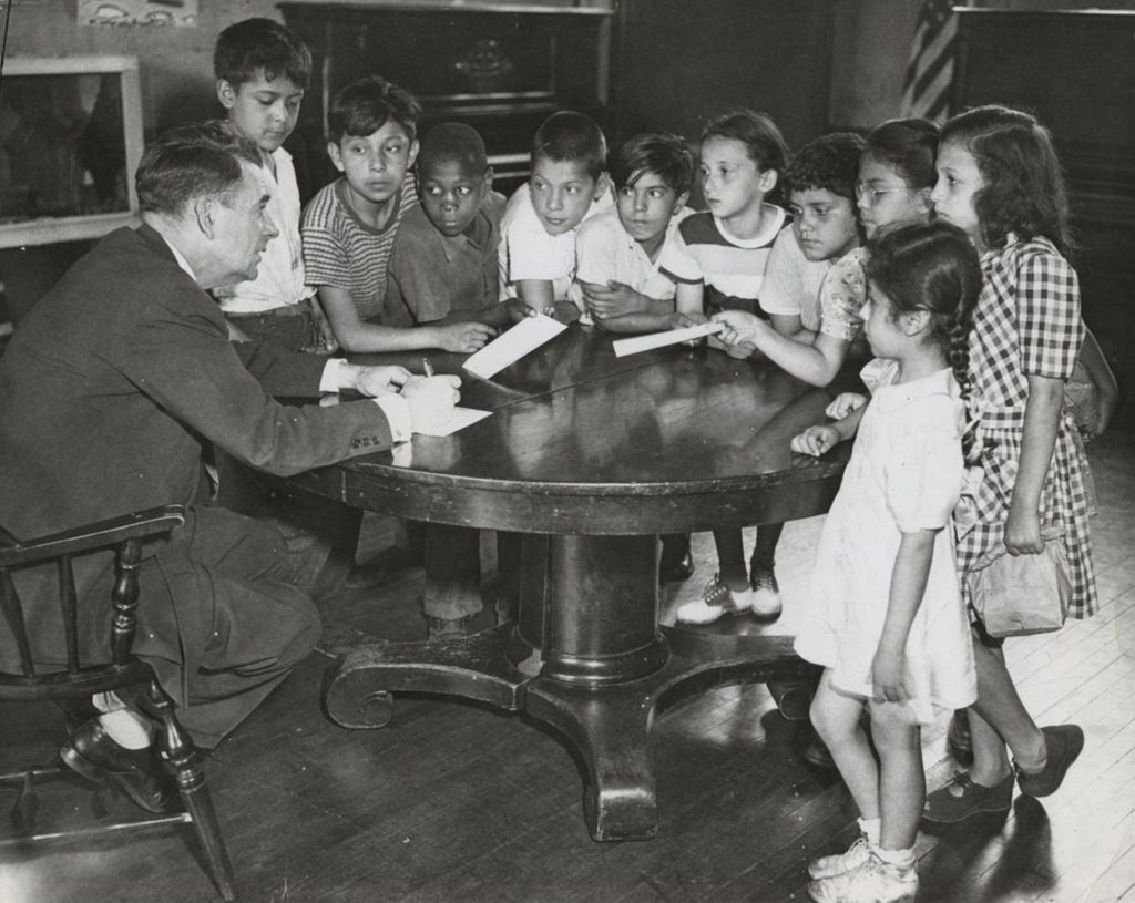 Hull-House Head Resident Russell W. Ballard signing summer camp registration forms for children around a table