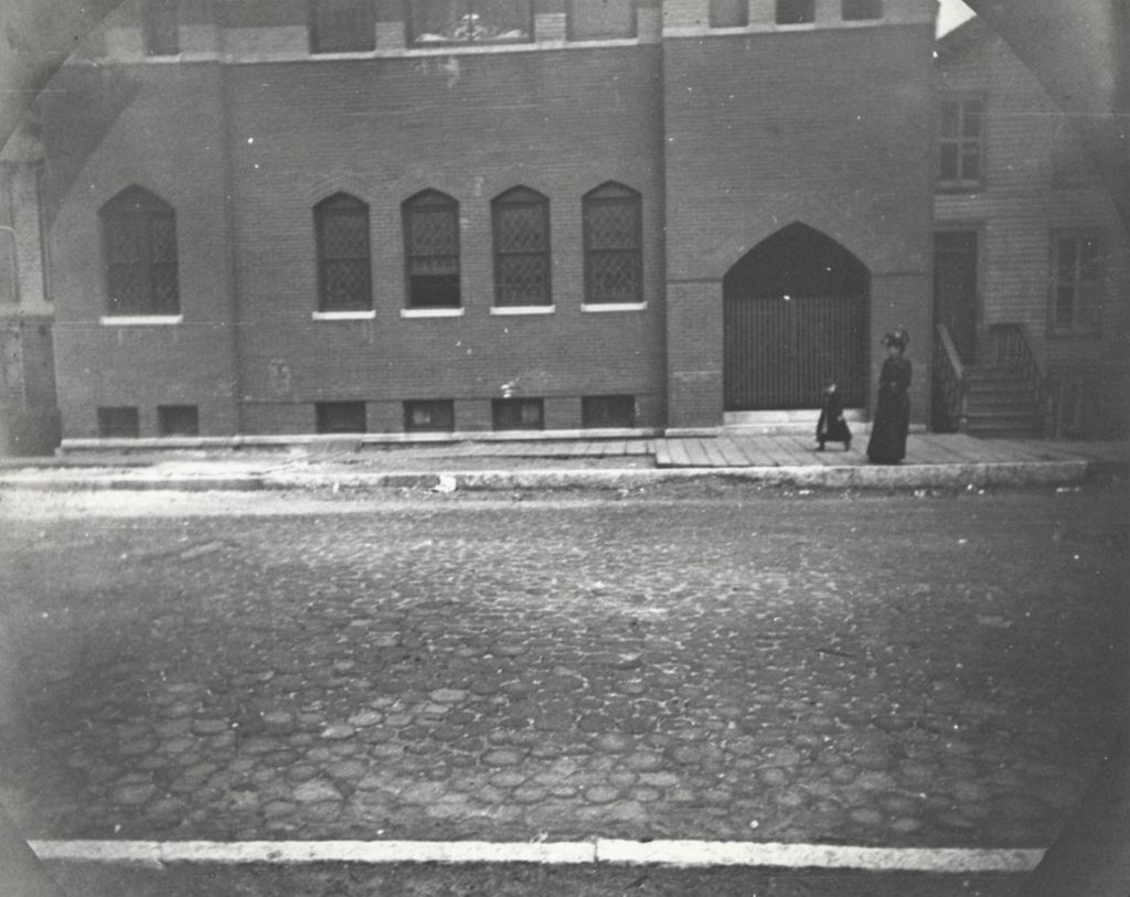 Miniature of Woman and child walking on sidewalk in front of a large brick building in a neighborhood near Hull-House