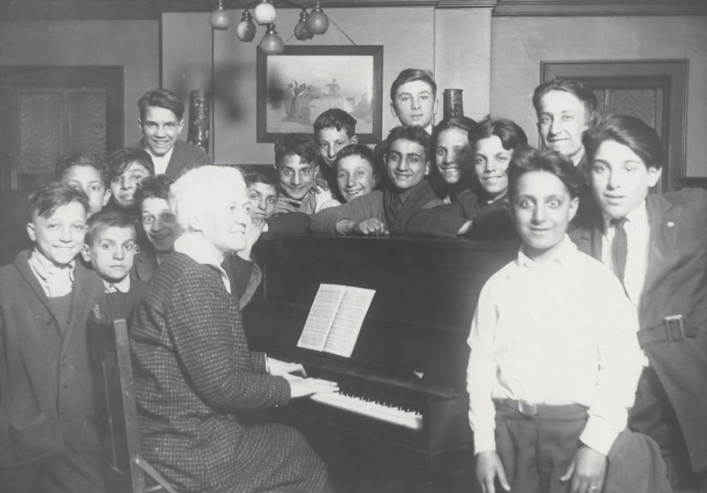 Music teacher at piano surrounded by large group of boys