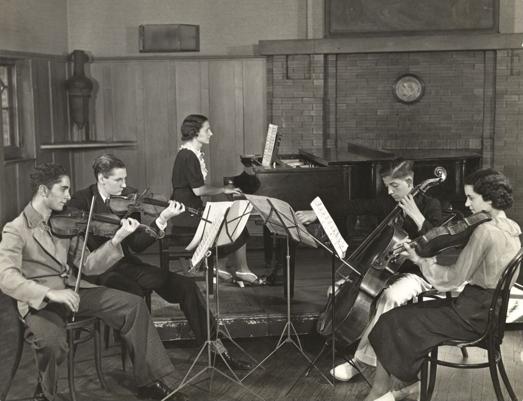 Four young musicians playing violins and cello while accompanied by woman on piano in Resident's Dining Hall