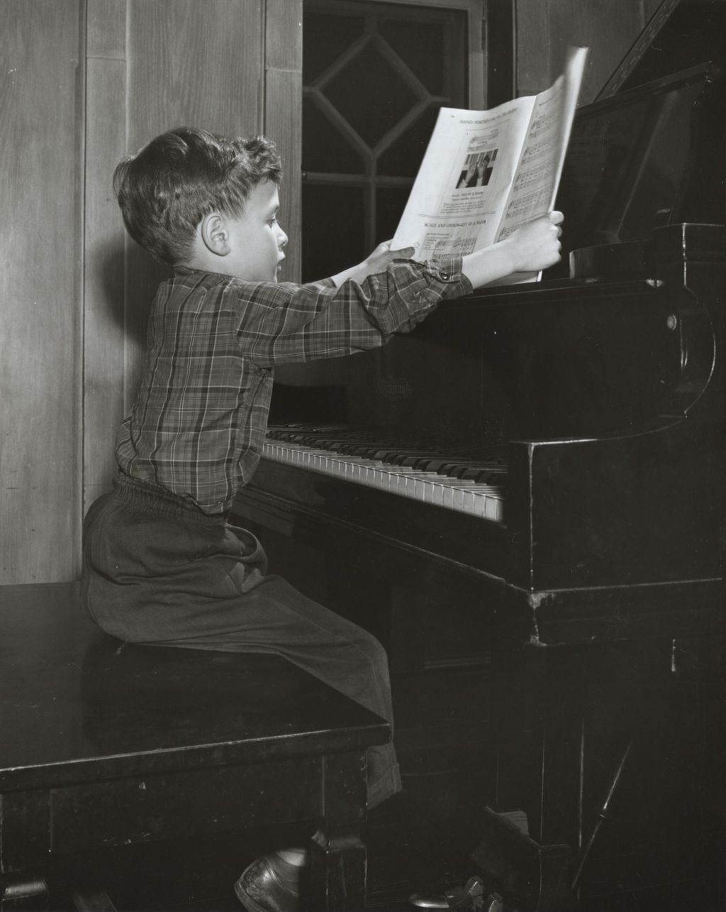 Boy sitting at piano opening sheet music at Hull-House Music School