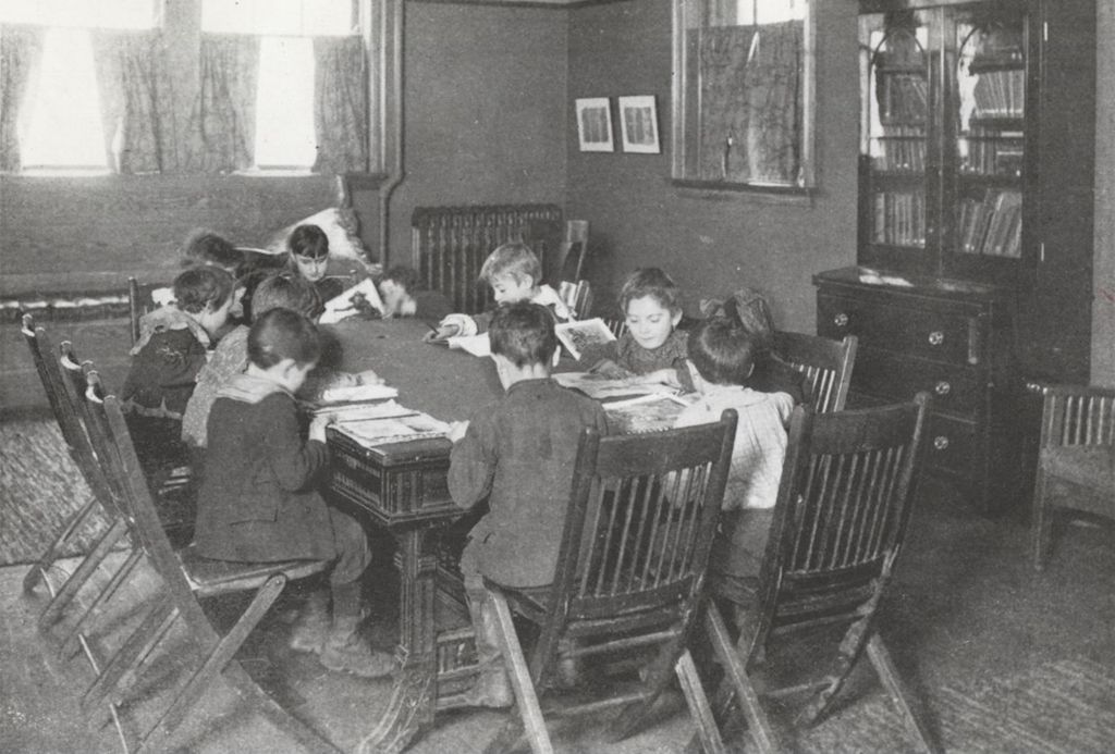 Miniature of Children sitting reading around a table in a reception room at Hull-House