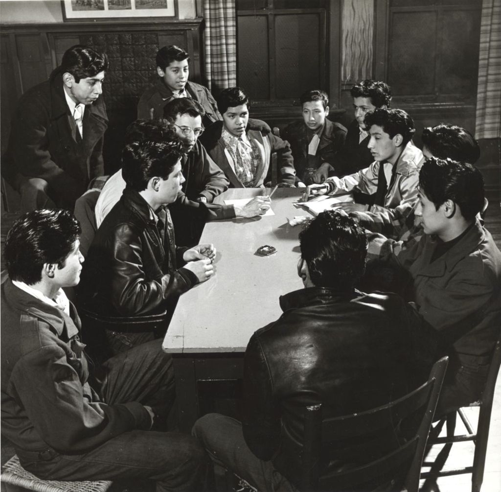 Twelve young men sit around a table with an advisor