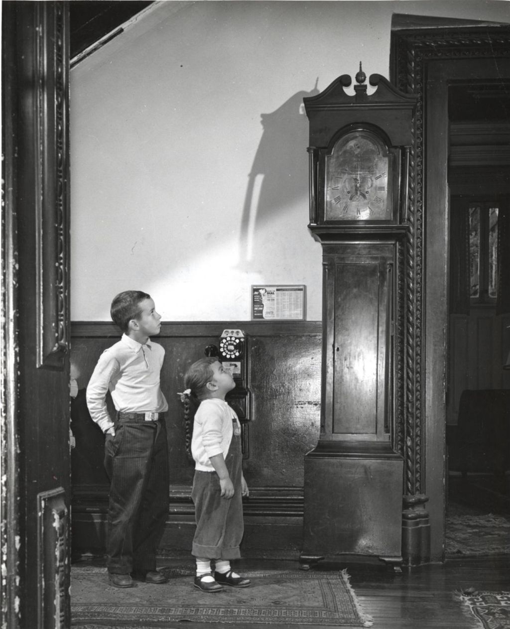 Boy and girl looking up at grandfather clock