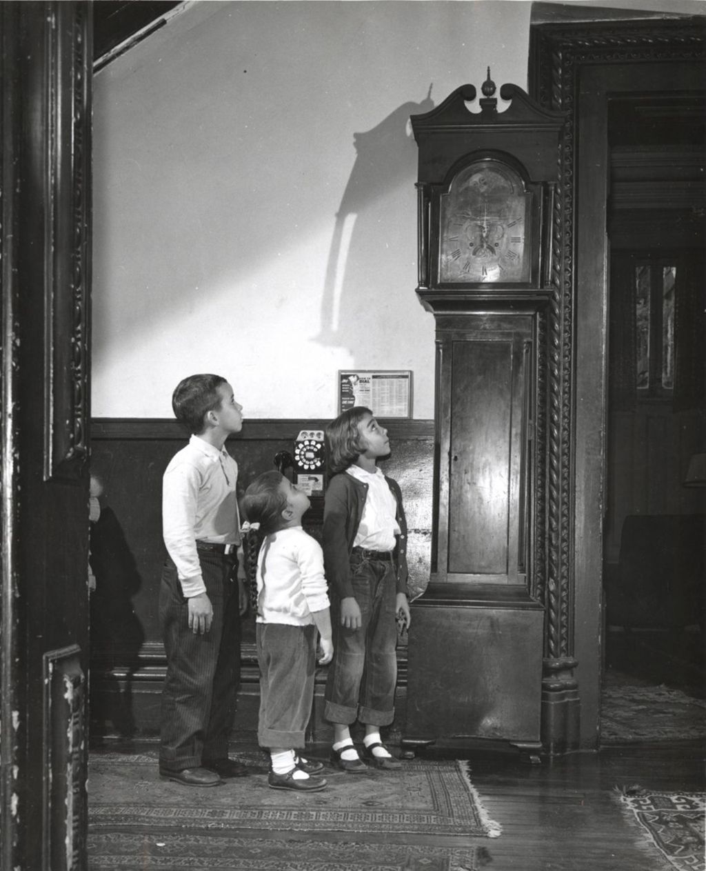 Three children looking up at grandfather clock