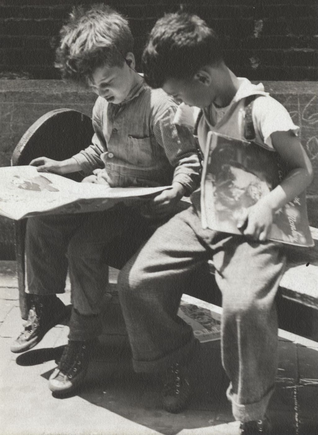 Two boys sitting outside on bench reading