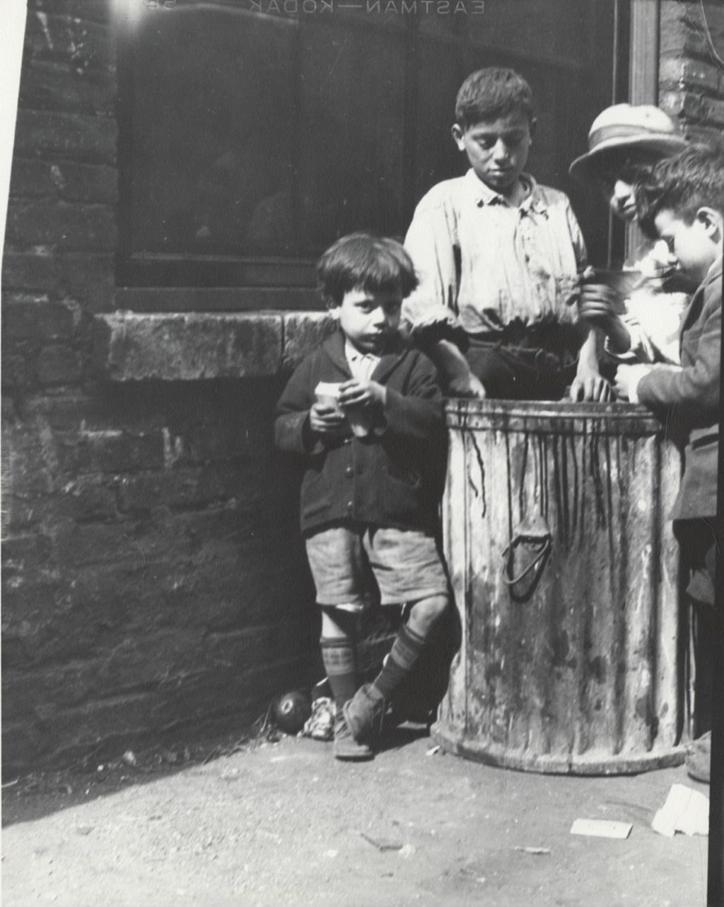 Four boys surround a garbage can in alley