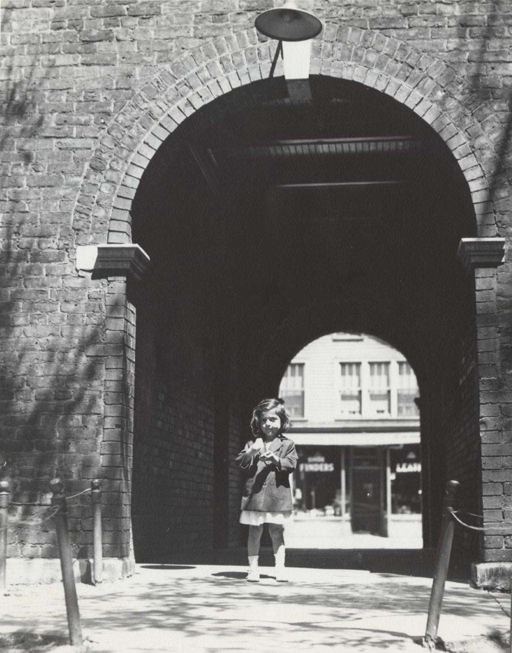 Girl (Lupe Ramos) standing in front of archway in Hull-House quadrangle