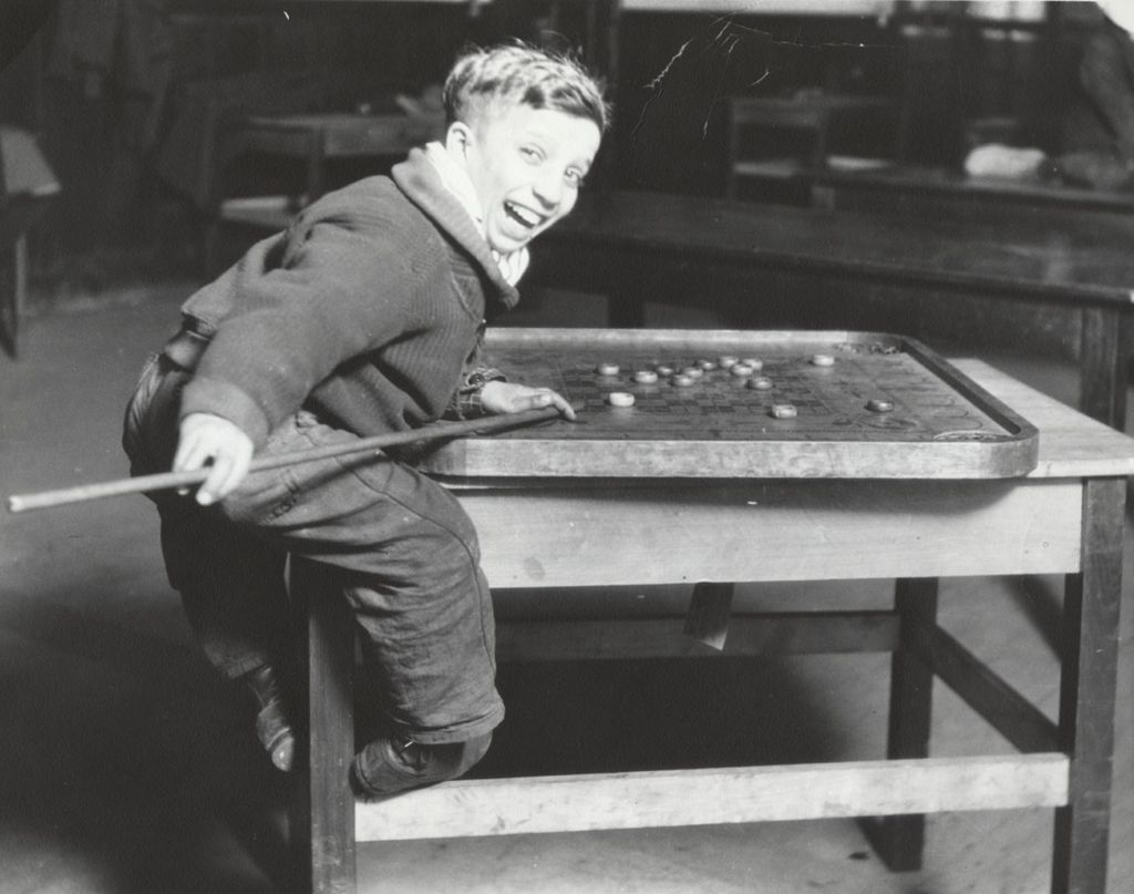 Boy playing carrom in Hull-House boys' game room