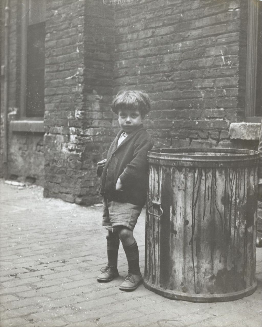 Young boy (Dom Esposito) standing next to garbage can in alley