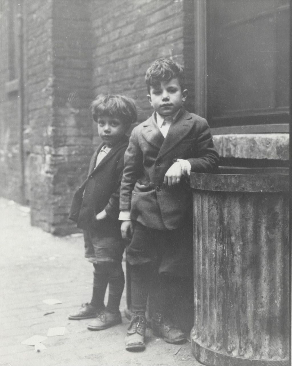 Two boys standing next to garbage can in alley