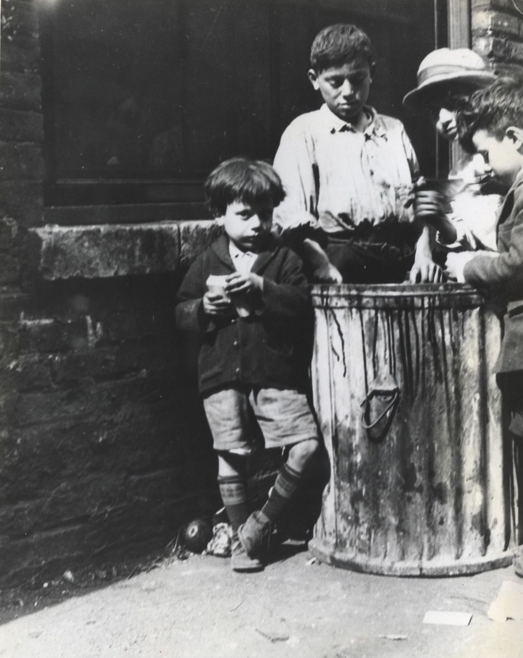 Four boys surround a garbage can in alley