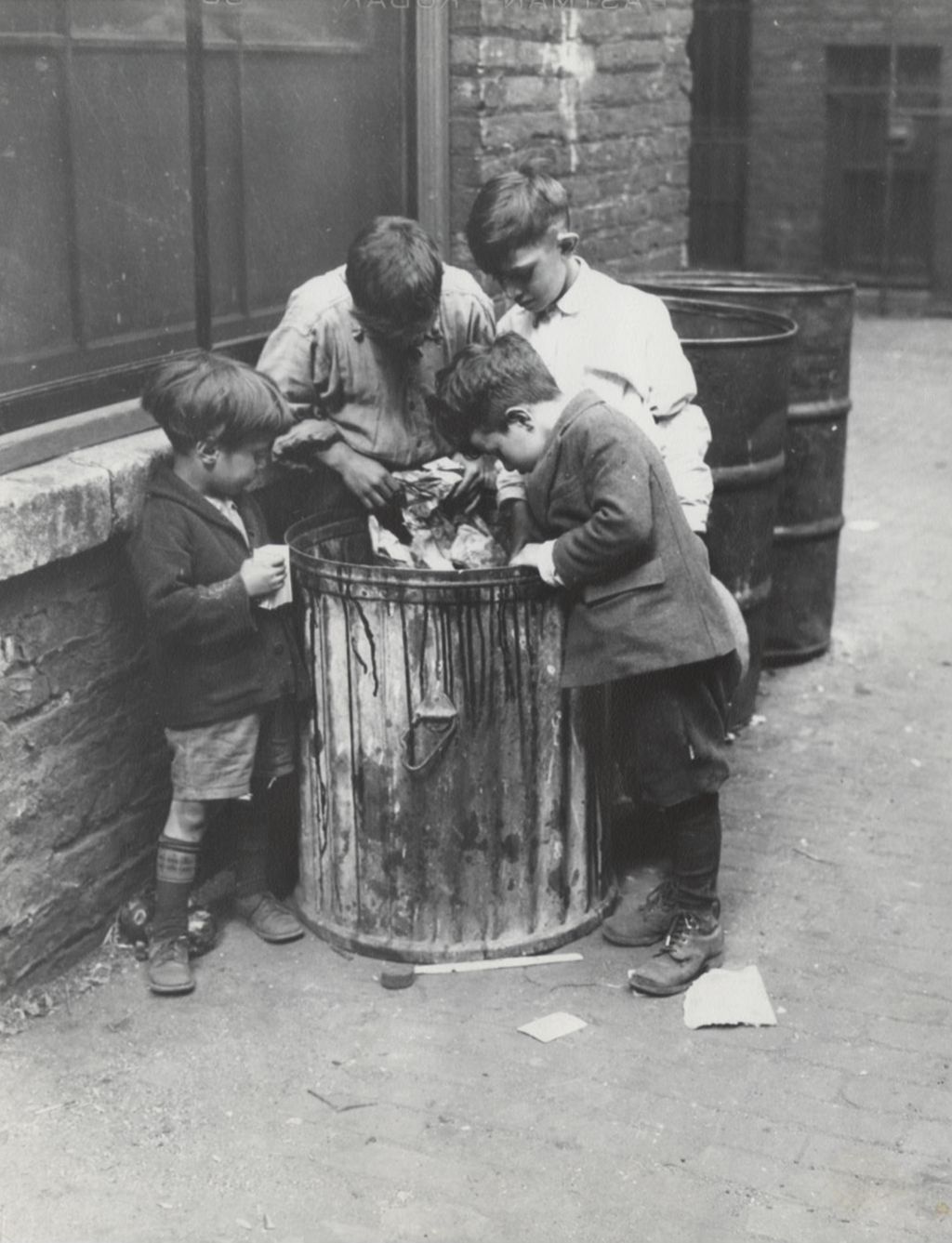Four boys digging through garbage can in alley