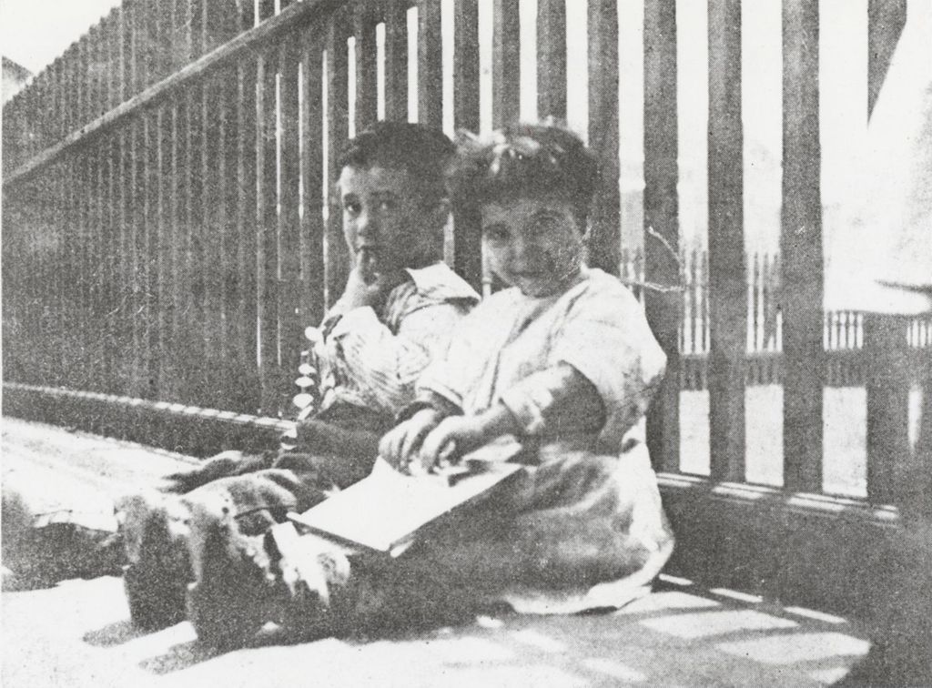 Two children sitting against the fence outside of Hull-House