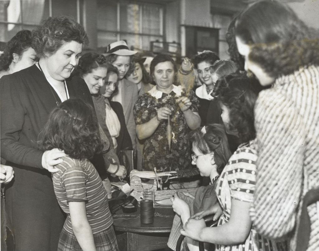 Girl knitting with Charlotte Carr and others looking on